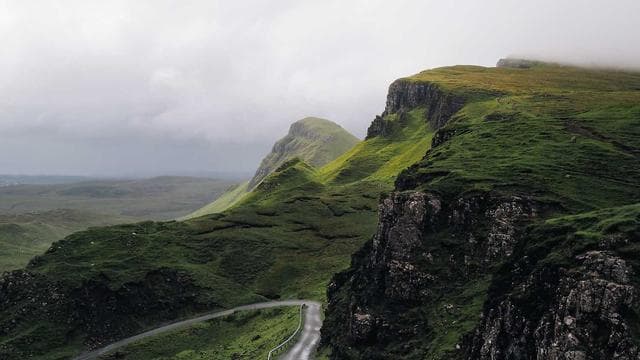 A cinematic landscape of a winding road through green Highland mountains